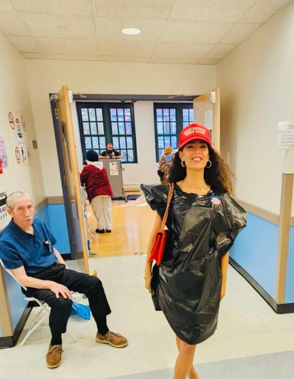 Sophie Sassoon wearing a MAGA hat and a black trash bag as a dress, standing in a hallway